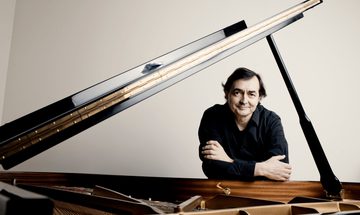Man leaning on open piano arms folded, facing camera and smiling