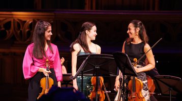 Three woman looking at each other smiling and holding stringed instruments