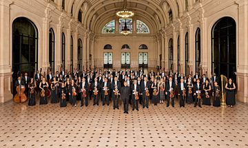 Symphony Orchestra standing together in grand hall holding their instruments