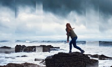 Woman standing on a rocks in ocean facing out to sea