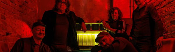 A group of 5 people sit and stand around a dark-lit red table.