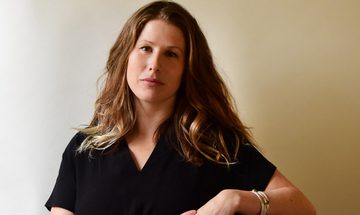 Woman in a black top leans casually to the side whilst looking at the camera