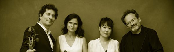 Four musicians in black and white clothing stand with their instruments