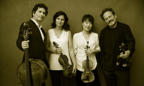Four musicians in black and white clothing stand with their instruments