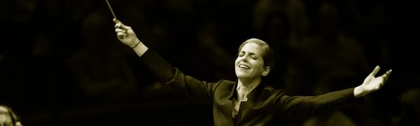 a conductor stands in front of the orchestra with her hands spread wide