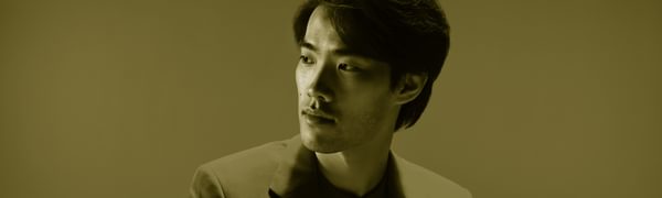 A man in a suit looks off to one side, he is bathed in red light