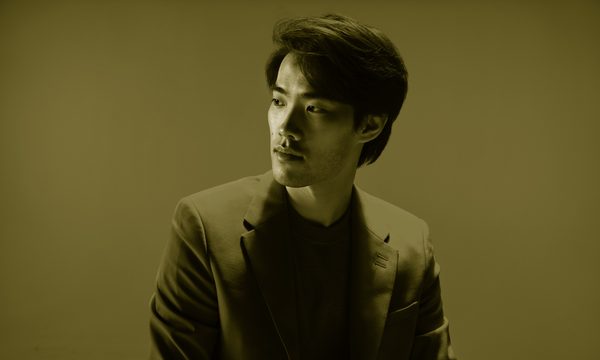 A man in a suit looks off to one side, he is bathed in red light