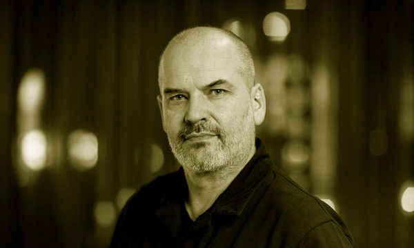 A man with a shaved head and greying beard looks at the viewer