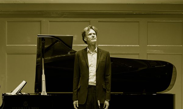 A man stands in front of a grand piano