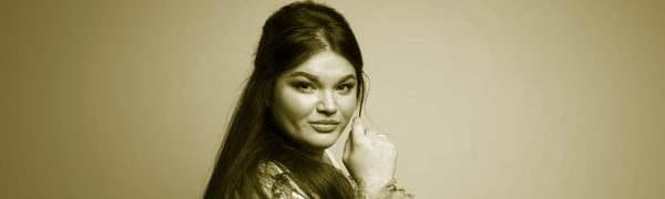 A woman with long brown hair in a pink and white gown looks over her shoulder with a knowing smile