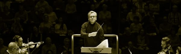 a conductor stands facing the orchestra with his baton across his chest