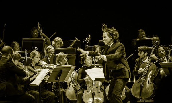 A conductor waves his arms enthusiastically before an orchestra