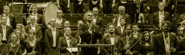 a conductor stands on the platform facing the audience his hands together in gratitude