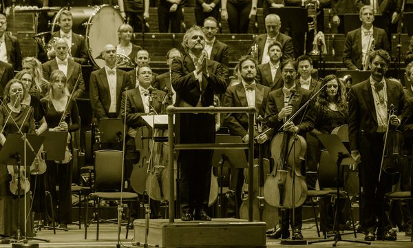 a conductor stands on the platform facing the audience his hands together in gratitude