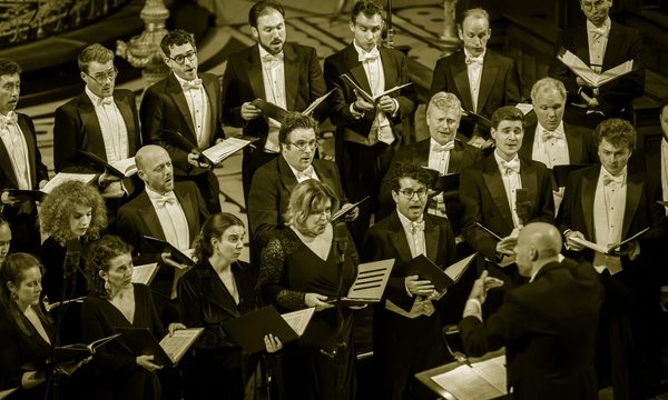 A choir dressed in formal wear sings in front of their conductor.