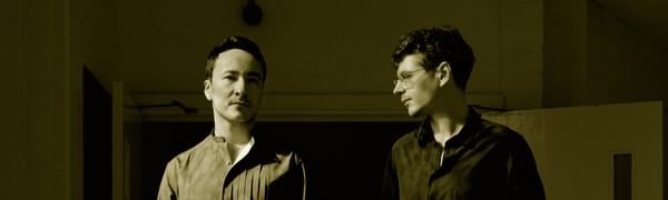 two men stand next to each other with a red background