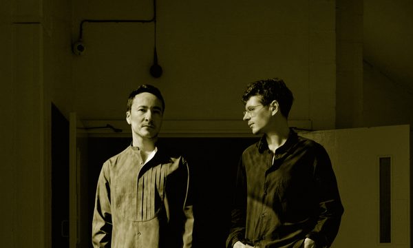 two men stand next to each other with a red background