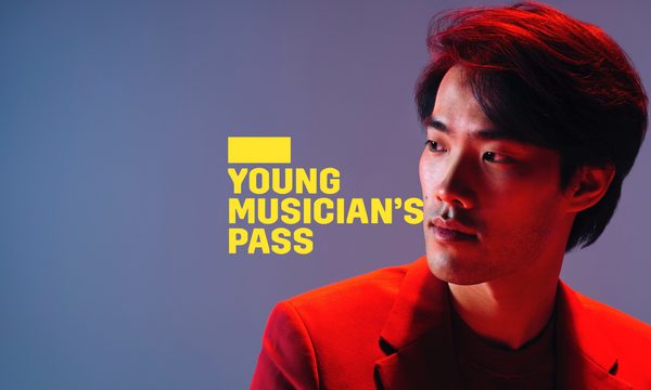 A yellow logo reading Young Musician's Pass overlays a man in a suit looking off to one side, he is bathed in red light