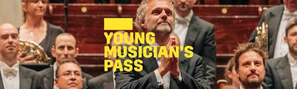 a A yellow logo reading Young Musician's Pass overlays a conductor standing on the platform facing the audience his hands together in gratitude