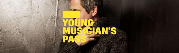 A yellow logo reading Young Musician's Pass overlays a man standing in a black room facing the side. He is wearing a knitted jumper and black trousers.