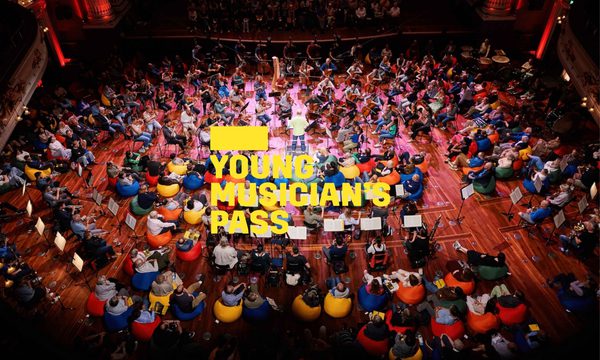 A yellow logo reading Young Musician's Pass overlays a birdseye view of an audience sitting on colourful beanbags with musicians placed among them and the conductor standing in the centre