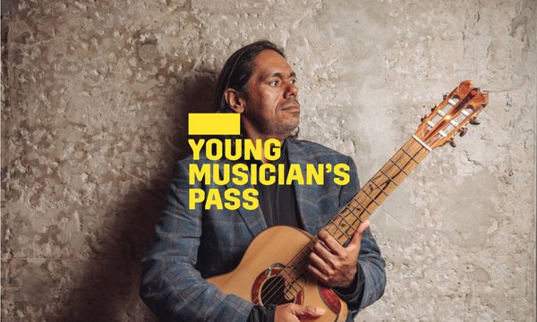A yellow logo reading Young Musician's Pass overlays a man standing in front of a stone wall holding a guitar and looking to the side.