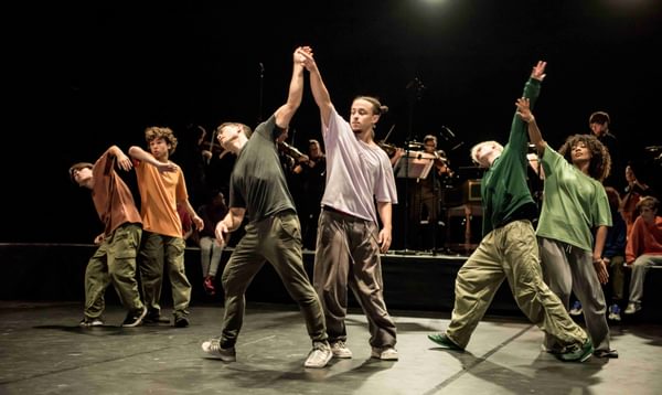 Dancers in casual t-shirts perform on stage, moving in three pairs.
