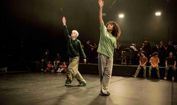 Two dancers in green shirts, their hands are extended to the ceiling.