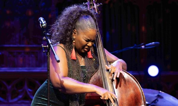 A woman plays the double bass by plucking the strings. Her face is strained in concentration.