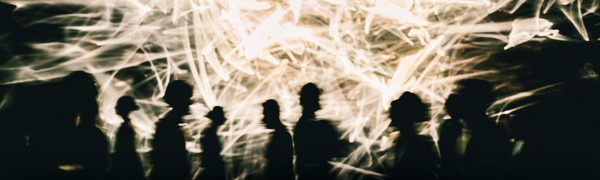 People are silhouetted against a screen showing white sparks and lines.