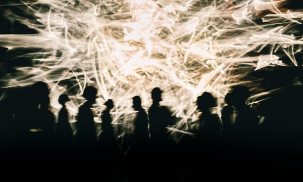 People are silhouetted against a screen showing white sparks and lines.