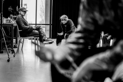 Black and white image of two members of the production team sat resting, the arms of another person are in the foreground.