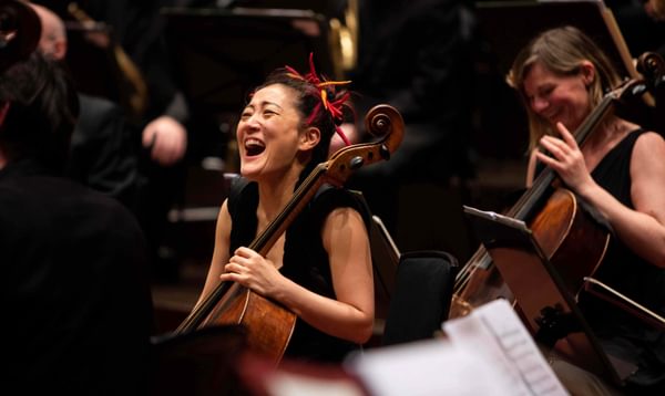 A female cellist within an orchestra laughs