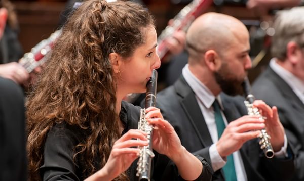 A woman with long brown hair plays a flute