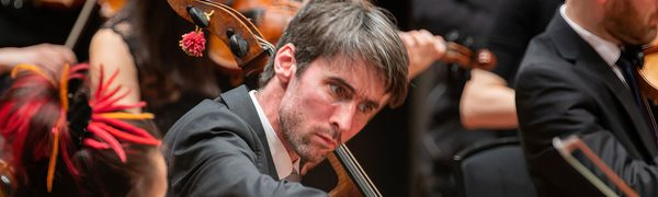 A cellist cocks his head, concentrating on playing his instrument.