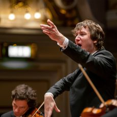 A conductor with his arm raised and mouth open.