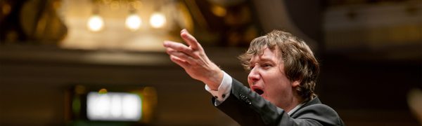 A conductor with his arm raised and mouth open.