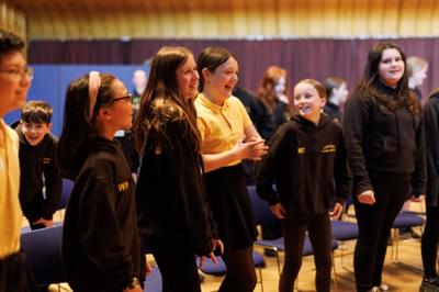 School children stand up from their seats smiling and laughing.