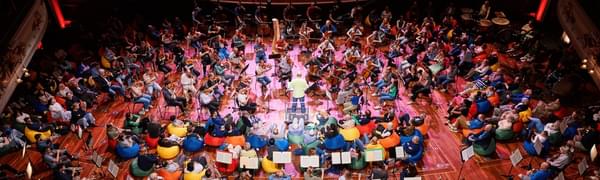 A birdseye view of an audience sitting on colourful beanbags with musicians placed among them and the conductor standing in the centre