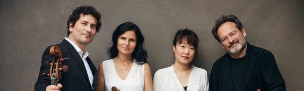 Four musicians in black and white clothing stand with their instruments