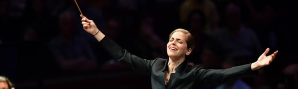 a conductor stands in front of the orchestra with her hands spread wide