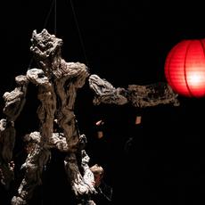 A large puppet with a rough rocky texture is being held up by 4 people. A red paper lantern hangs in front of them.