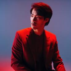 A man in a suit looks off to one side, he is bathed in red light