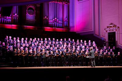 A large choir stand on stage in front of a large organ, with the chorus director standing before them