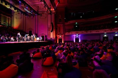 An audience sitting on brightly coloured beanbags watching a group of musicians perform on stage.