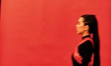 A blurred image of a woman in a black dress walking by a red wall