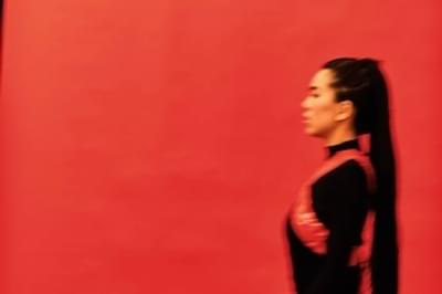 A blurred image of a woman in a black dress walking by a red wall
