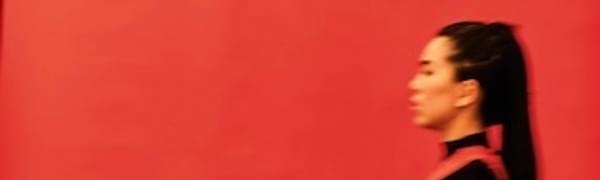 A blurred image of a woman in a black dress walking by a red wall