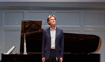 A man stands in front of a grand piano