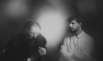 Two men sit looking away from the camera, obscured by bright lights